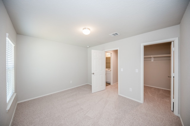 unfurnished bedroom with light colored carpet, a walk in closet, and a closet