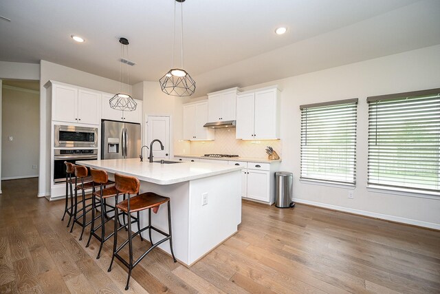 kitchen with white cabinets, decorative light fixtures, stainless steel appliances, and an island with sink