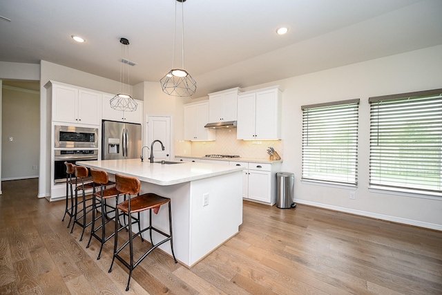 kitchen with appliances with stainless steel finishes, a kitchen island with sink, hanging light fixtures, and white cabinets