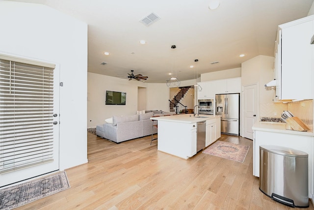 kitchen with pendant lighting, light hardwood / wood-style flooring, white cabinetry, stainless steel appliances, and a center island with sink