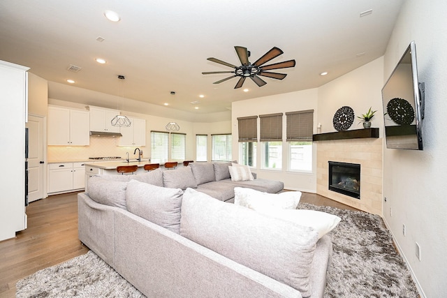 living room with a tile fireplace, ceiling fan, sink, and light wood-type flooring