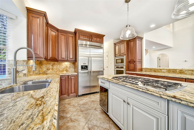 kitchen featuring backsplash, sink, hanging light fixtures, built in appliances, and light stone counters