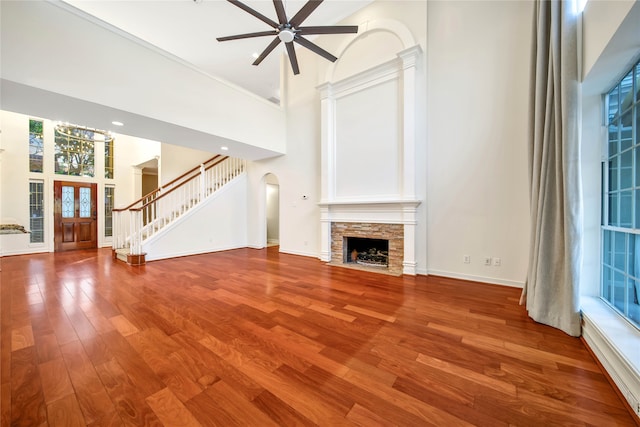 unfurnished living room with ceiling fan, a fireplace, a towering ceiling, and wood-type flooring