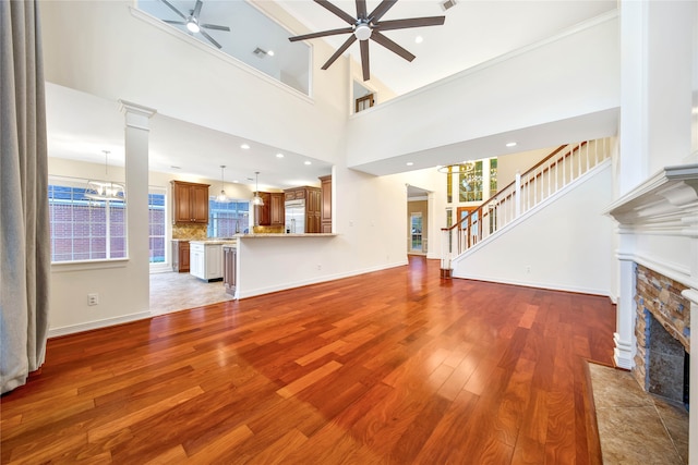 unfurnished living room featuring a stone fireplace, ceiling fan with notable chandelier, a high ceiling, and hardwood / wood-style flooring