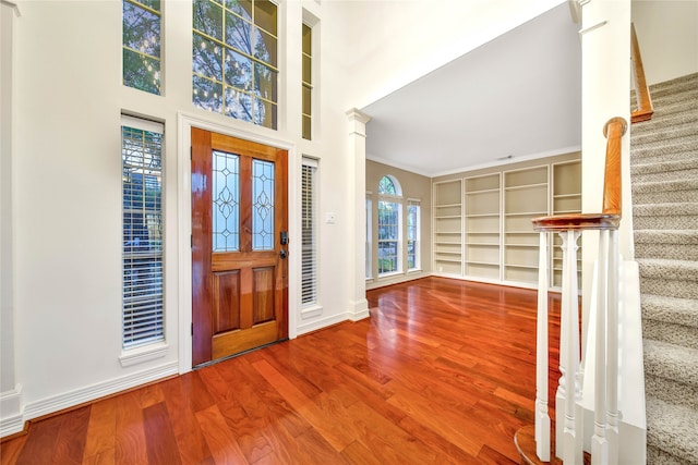 foyer entrance with wood-type flooring, ornamental molding, and a high ceiling