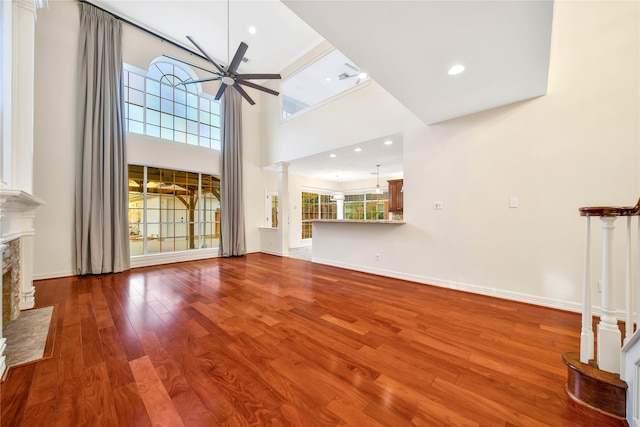 unfurnished living room with hardwood / wood-style flooring, ceiling fan, beam ceiling, and a towering ceiling