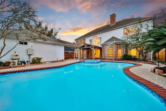 pool at dusk featuring an in ground hot tub