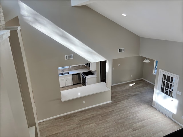 unfurnished living room featuring sink, high vaulted ceiling, and light hardwood / wood-style flooring