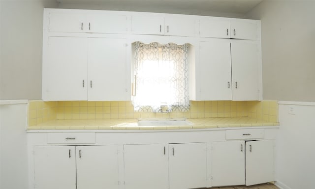 kitchen with tile countertops, white cabinetry, tasteful backsplash, and sink