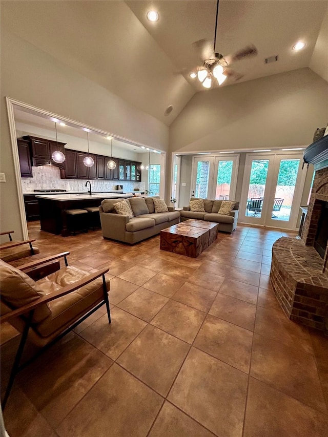 tiled living room featuring ceiling fan, high vaulted ceiling, and a brick fireplace