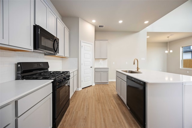 kitchen featuring light wood-type flooring, sink, black appliances, a center island with sink, and an inviting chandelier