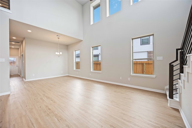 unfurnished living room featuring a notable chandelier, plenty of natural light, light hardwood / wood-style floors, and a high ceiling