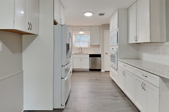 kitchen with tasteful backsplash, white appliances, sink, light hardwood / wood-style flooring, and white cabinets