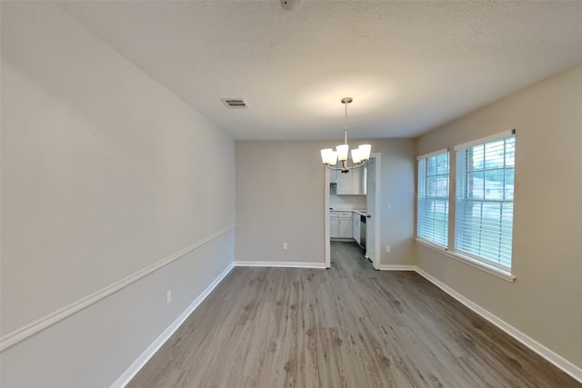 unfurnished dining area with light wood-type flooring, a textured ceiling, and a chandelier