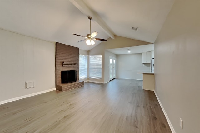 unfurnished living room featuring a brick fireplace, ceiling fan, lofted ceiling with beams, and light wood-type flooring