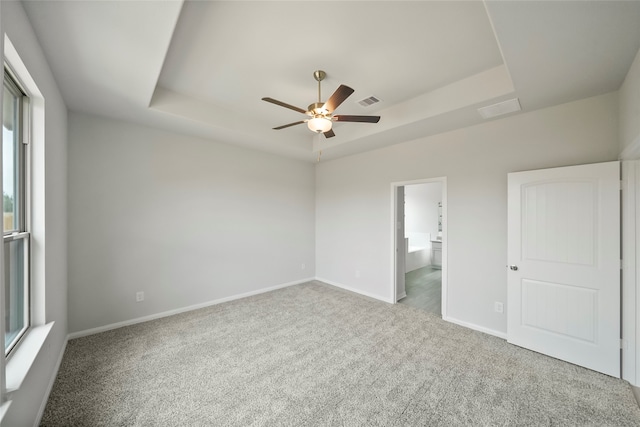 unfurnished bedroom with a tray ceiling, ceiling fan, carpet, and ensuite bathroom