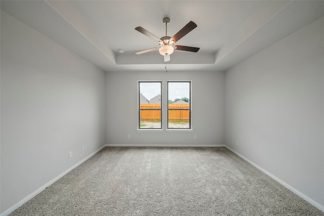 carpeted spare room featuring a raised ceiling and ceiling fan