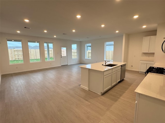 kitchen featuring sink, a kitchen island with sink, white cabinetry, stainless steel dishwasher, and light wood-type flooring