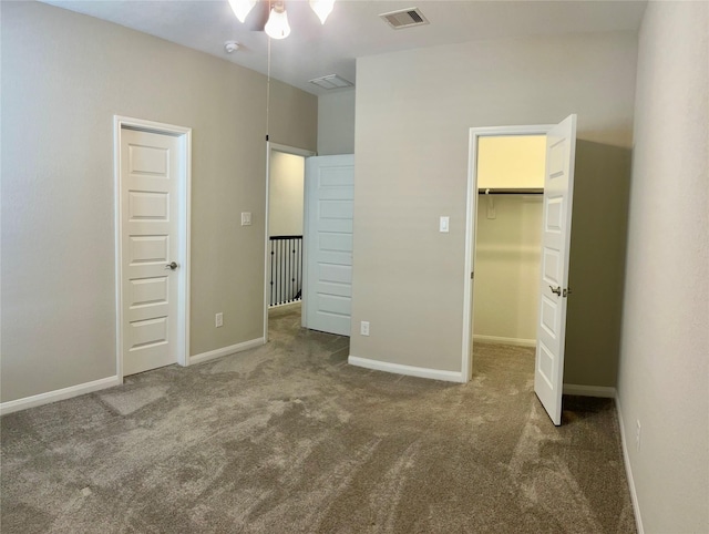 unfurnished bedroom with ceiling fan, dark carpet, a spacious closet, and a closet