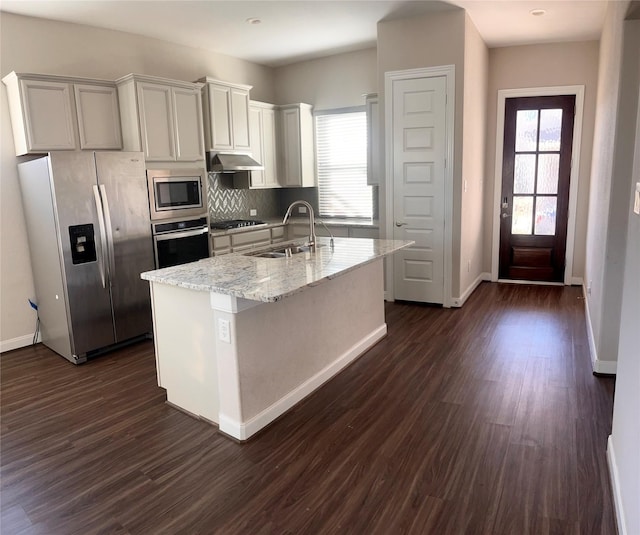 kitchen featuring sink, dark wood-type flooring, light stone counters, an island with sink, and appliances with stainless steel finishes