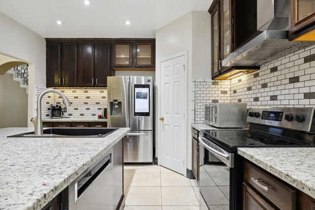 kitchen featuring light stone counters, sink, stainless steel appliances, and wall chimney range hood