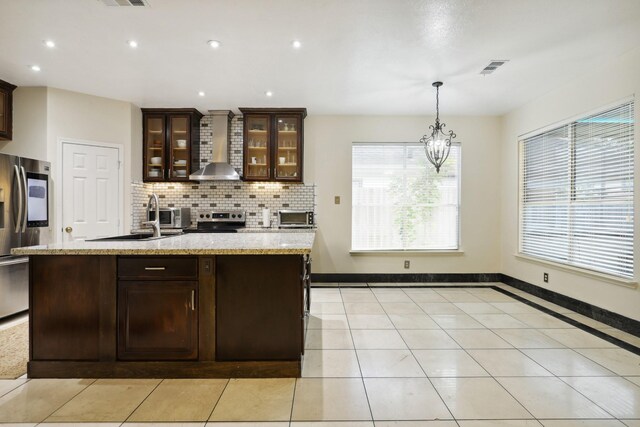 kitchen featuring dark brown cabinetry, a wealth of natural light, wall chimney range hood, and appliances with stainless steel finishes