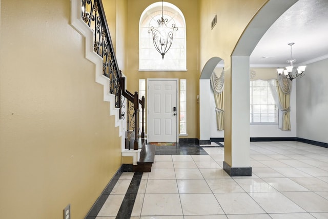 entrance foyer featuring a chandelier, a towering ceiling, ornamental molding, and light tile patterned flooring