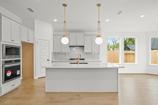 kitchen featuring stainless steel appliances, light hardwood / wood-style floors, a center island with sink, and sink