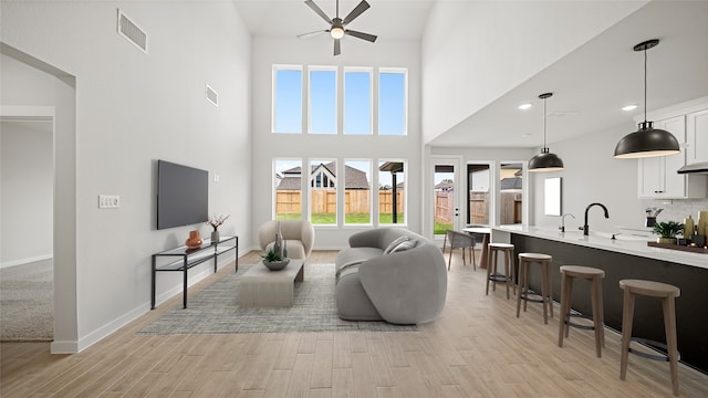 living room with ceiling fan, plenty of natural light, a towering ceiling, and light wood-type flooring