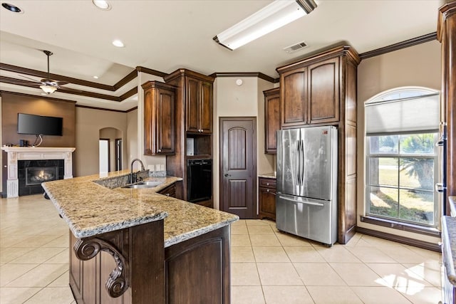 kitchen featuring sink, ceiling fan, stainless steel fridge, kitchen peninsula, and a tiled fireplace