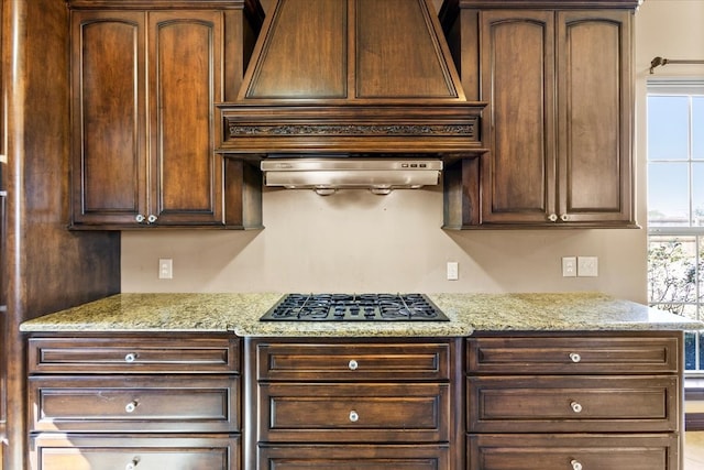 kitchen featuring premium range hood, black gas stovetop, light stone counters, and ventilation hood