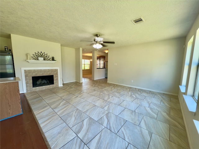 unfurnished living room with ceiling fan, a textured ceiling, and a tiled fireplace