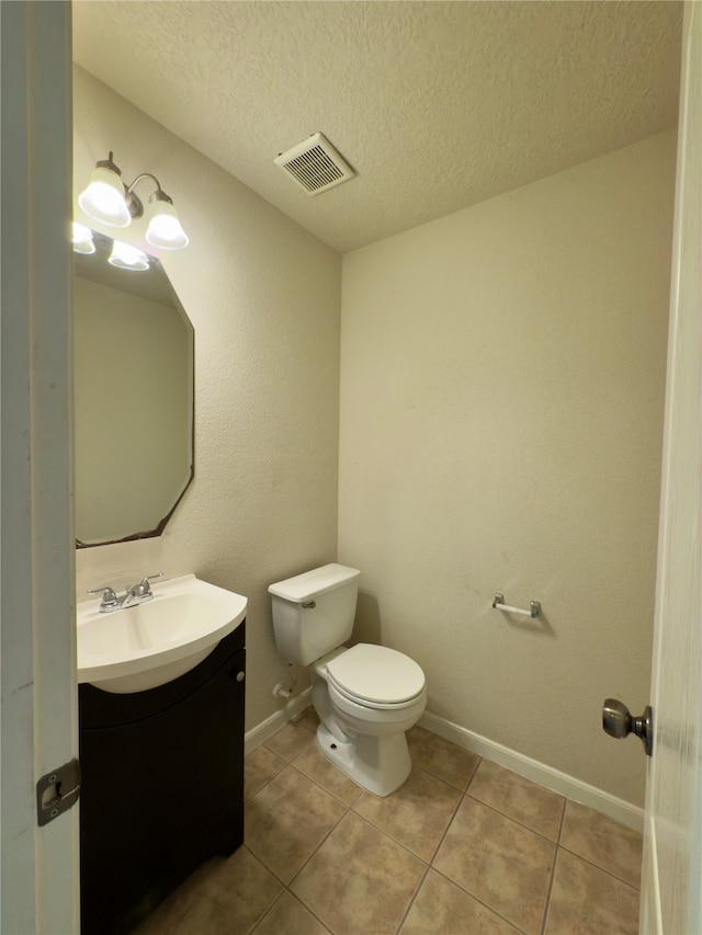 bathroom with tile patterned flooring, vanity, toilet, and a textured ceiling