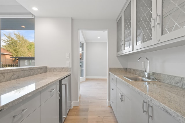 kitchen featuring wine cooler, light stone counters, sink, and light wood-type flooring