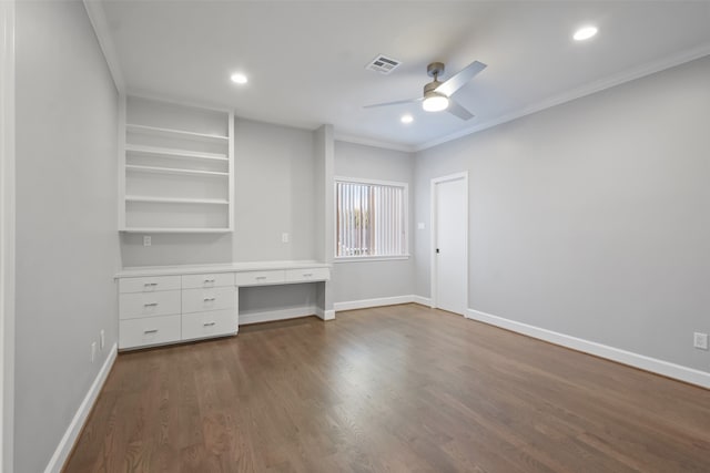 unfurnished bedroom with ceiling fan, dark wood-type flooring, built in desk, and ornamental molding