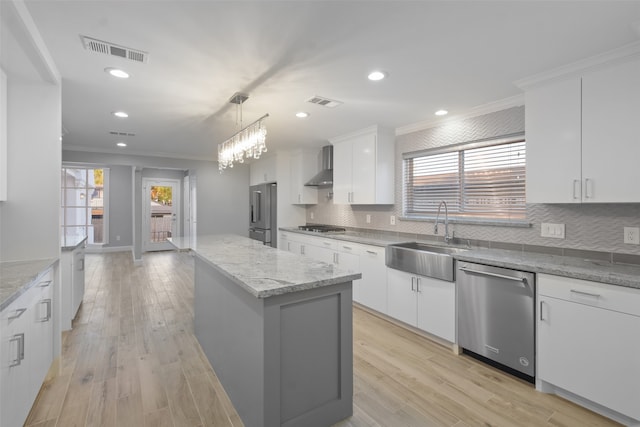 kitchen with appliances with stainless steel finishes, a kitchen island, wall chimney range hood, sink, and white cabinetry