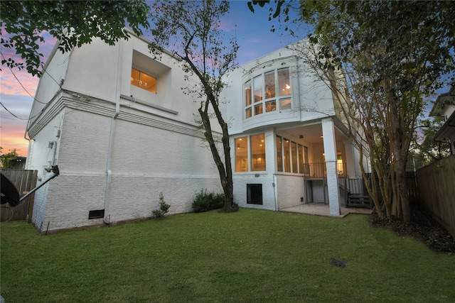 back house at dusk featuring a lawn