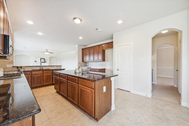 kitchen with ceiling fan, sink, tasteful backsplash, dark stone counters, and a kitchen island