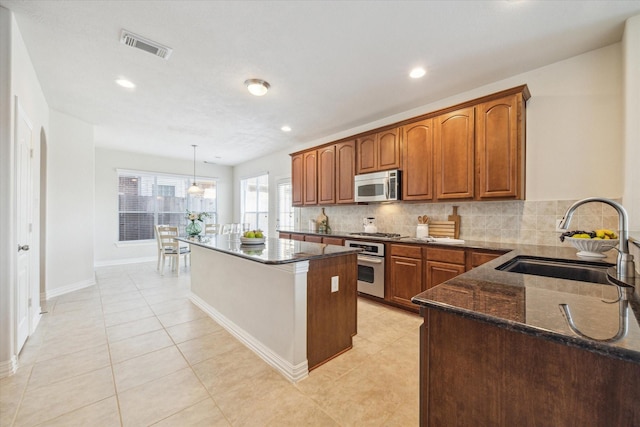 kitchen featuring backsplash, stainless steel appliances, sink, decorative light fixtures, and a center island