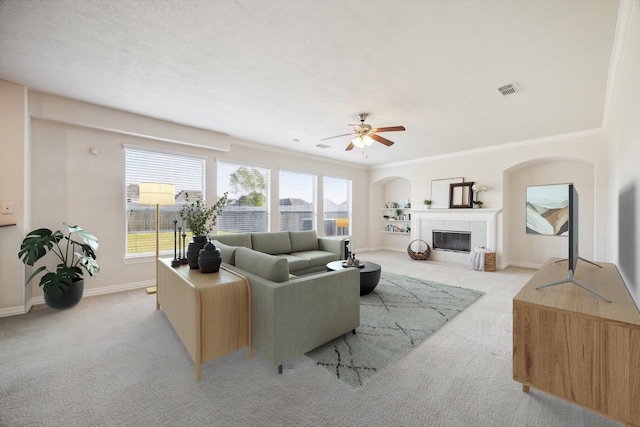 living room with a tile fireplace, light colored carpet, ceiling fan, and crown molding