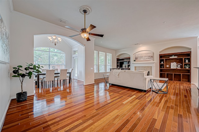 living room with built in shelves, light hardwood / wood-style floors, and ceiling fan with notable chandelier