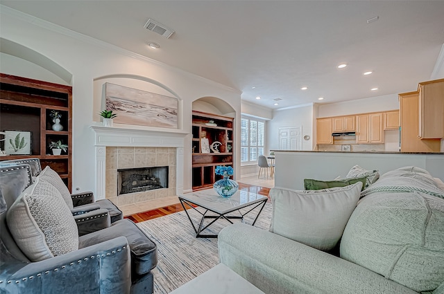 living room featuring a fireplace, crown molding, light hardwood / wood-style flooring, and built in features