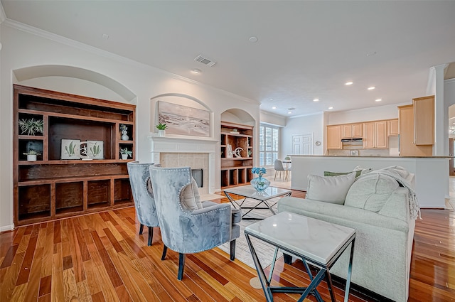 living room with built in shelves, light hardwood / wood-style floors, crown molding, and a fireplace