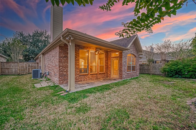 back house at dusk featuring a lawn, central air condition unit, and a patio