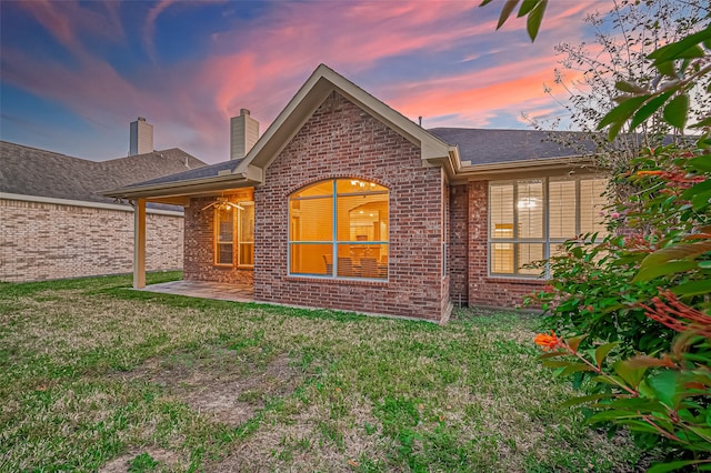 back house at dusk featuring a lawn and a patio