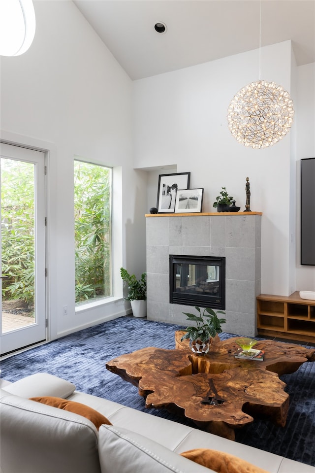 living room with a chandelier, a healthy amount of sunlight, high vaulted ceiling, and a tiled fireplace