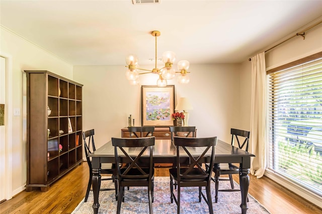 dining room featuring a healthy amount of sunlight, wood-type flooring, and an inviting chandelier