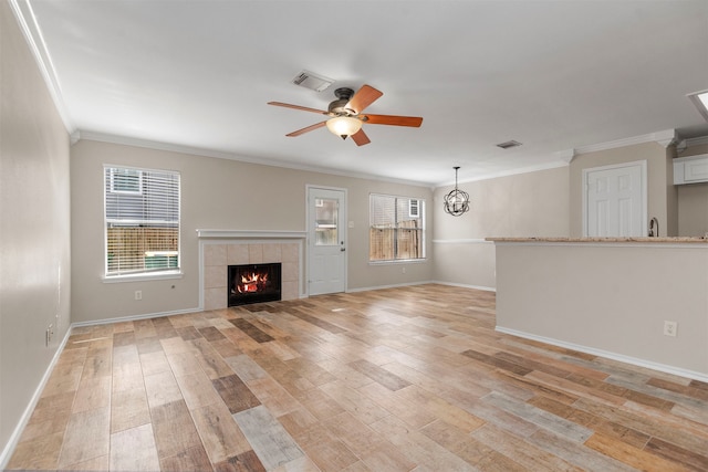 unfurnished living room with ceiling fan with notable chandelier, light wood-type flooring, crown molding, and a tile fireplace