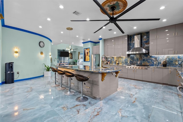 kitchen featuring a kitchen breakfast bar, gray cabinets, ceiling fan, and wall chimney range hood