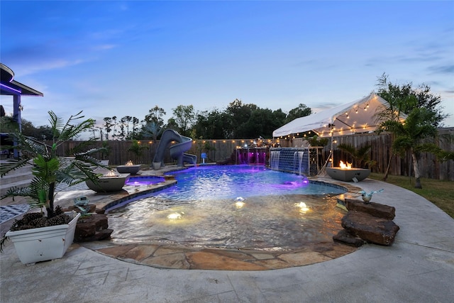 pool at dusk with pool water feature and a water slide